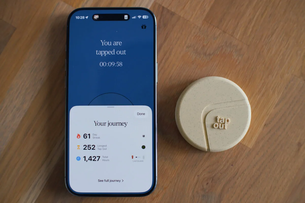 De Tap Out Home naast een telefoon die op pauze staat, op een houten bureau